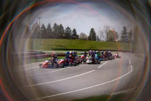 26HRKC1CKN1227 Elementor Hosted Website Elementor Hosted Website Group of go-kart racers speeding around a track with barriers and grassy infield, framed by a rainbow-colored lens flare.