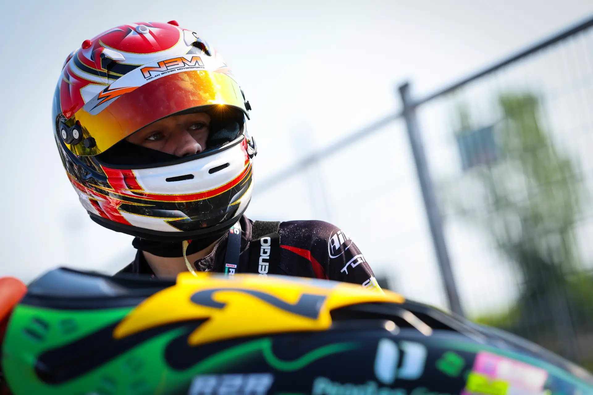 Close-up of a race car driver wearing a red, white, and yellow helmet, looking to the left.