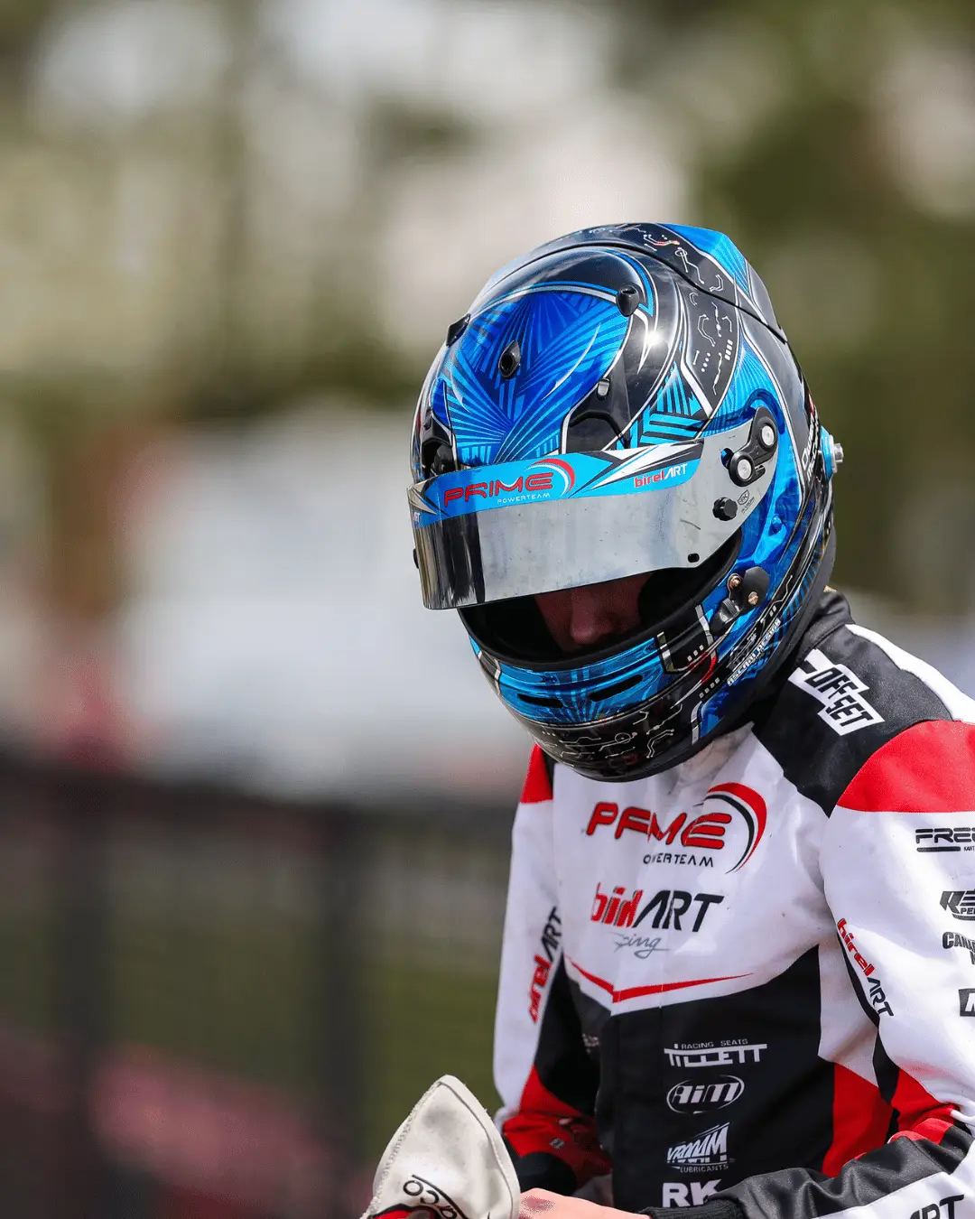 6 Elementor Hosted Website Motorsport racer wearing a blue patterned helmet and white-red racing suit with sponsor logos, preparing for a race.
